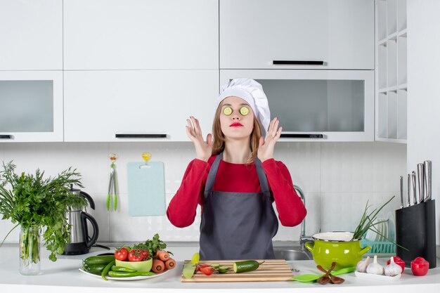 Front view female chef in cook hat putting cucumber slices on her eyes in kitchen