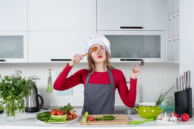 Front view female chef in cook hat putting wooden spoon in front of her eye