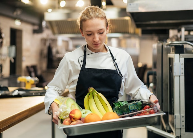 Front view of female chef holding tray with fruit