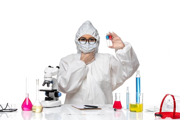 Front view female chemist in special protective suit holding empty flasks on white desk health virus chemistry covid