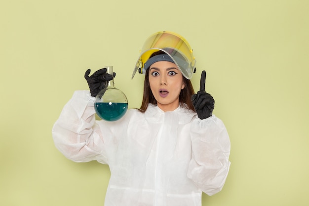 Free photo front view female chemist in special protective suit holding flask with blue solution on green surface