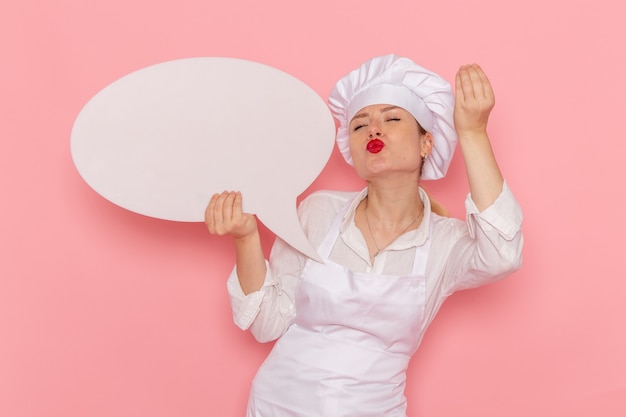 Free photo front view female confectioner in white wear holding white sign on pink wall confectionery sweet pastry