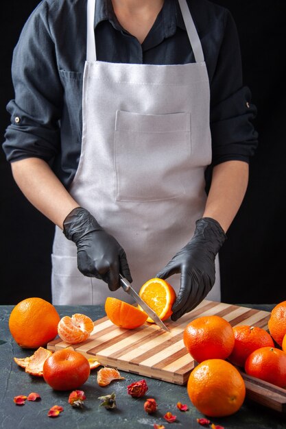 Front view female cook cutting orange on a dark drink salad health meal food job vegetable fruit diet