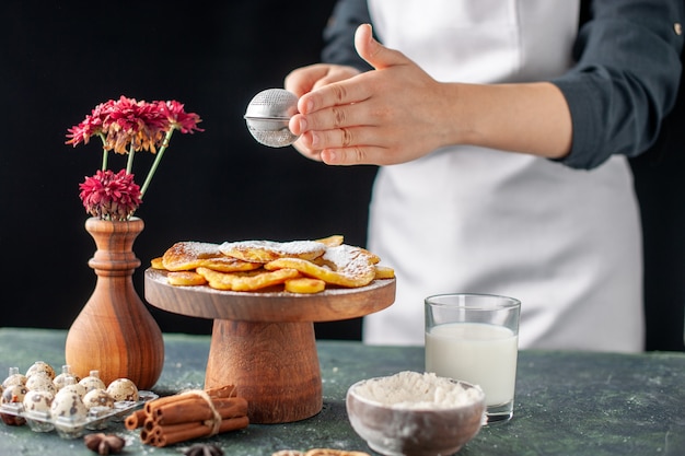 Front view female cook pouring sugar powder on dried pineapple rings on a dark fruit job pastry cake pie bakery cooking