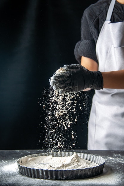 Free photo front view female cook pouring white flour into the pan on a dark egg cake bakery pastry cuisine dough pie hotcake kitchen