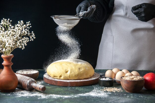 Front view female cook pouring white flour on raw dough on dark pastry job raw dough hotcake bakery pie oven