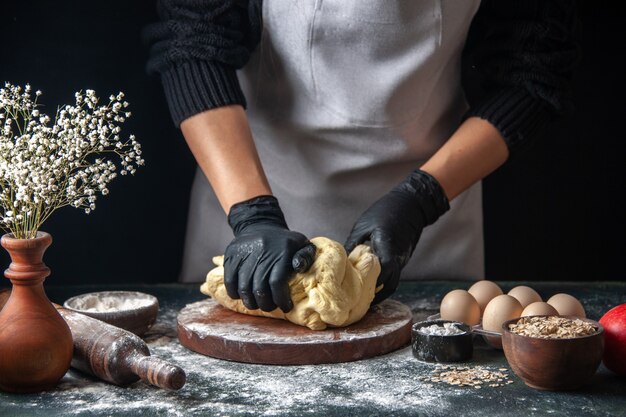 Front view female cook rolling out dough on dark job raw dough hotcake bakery pie oven pastry