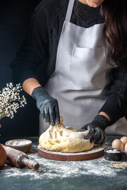 Front view female cook rolling out dough on the dark pastry job raw dough hotcake bakery pie oven