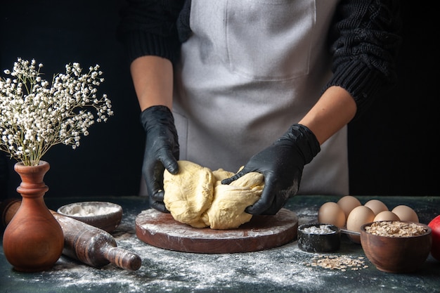 Front view female cook rolling out dough on dark pastry job raw dough hotcake bakery pie