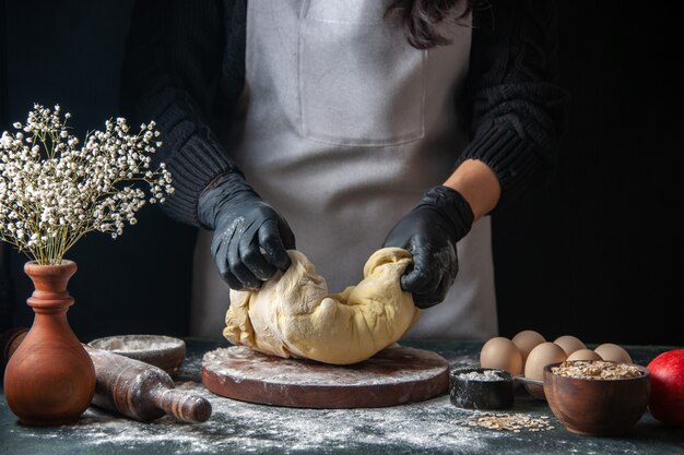 Front view female cook rolling out dough on dark pastry job raw dough hotcakes bakery pie oven