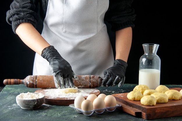 Front view female cook rolling out dough with flour on dark cake job oven hotcake dough bake pie worker egg cuisine