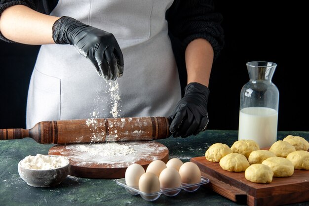 Front view female cook rolling out dough with flour on dark job cuisine hotcake raw dough bake cake pie worker egg