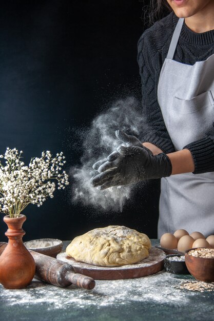 Front view female cook rolling out dough with flour on dark job dough bakery pie oven pastry hotcake