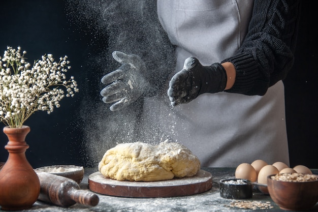 Front view female cook rolling out dough with flour on dark job raw dough bakery pie oven pastry hotcake