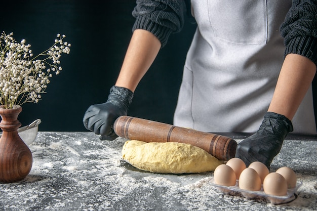 Front view female cook rolling out dough with rolling pin on the dark dough egg job bakery hotcake pastry kitchen cuisine