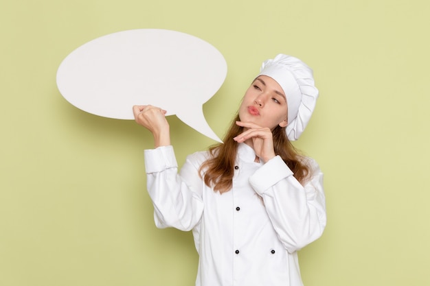 Free photo front view of female cook wearing white cook suit holding big sign and thinking on green wall