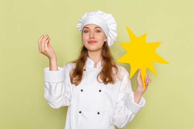 Free Photo front view of female cook wearing white cook suit holding a yellow sign on the green wall