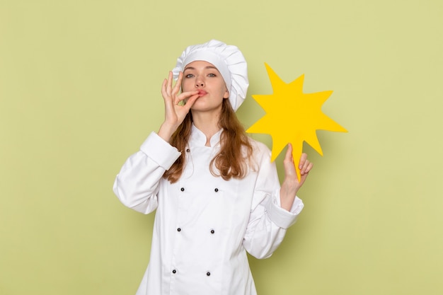 Free Photo front view of female cook wearing white cook suit holding yellow sign on green wall