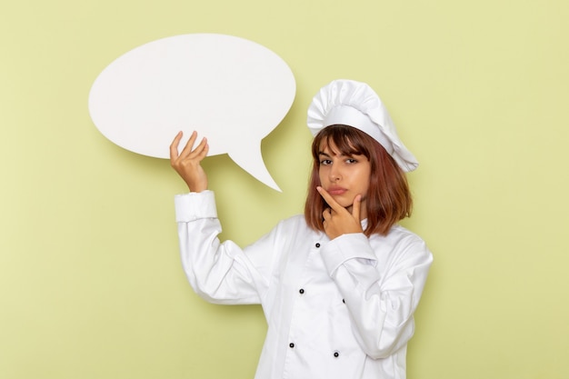 Free Photo front view female cook in white cook suit holding a big white sign on green surface