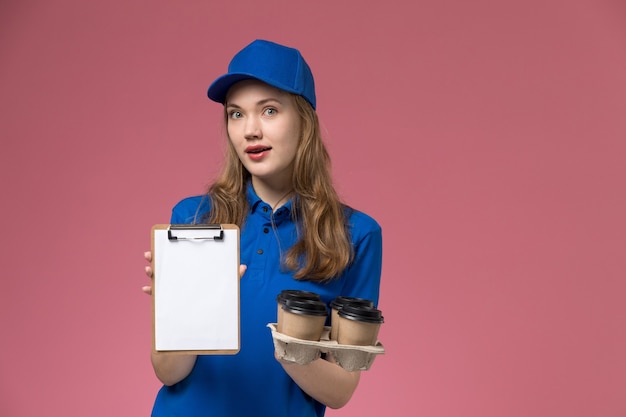 Free photo front view female courier in blue uniform holding notepad and delivery coffee cups on light desk service uniform company job