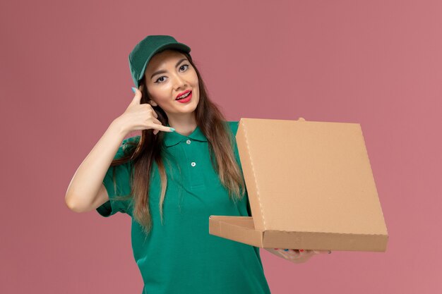 Front view female courier in green uniform holding food delivery box on pink wall company service uniform delivery work