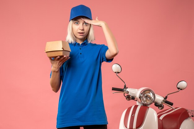 Front view female courier holding little food package on pink 