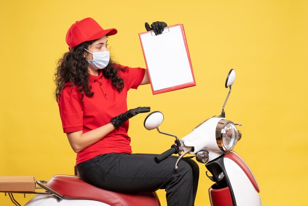 Front view female courier in mask holding file note on yellow background covid- job uniform worker service work pandemic delivery