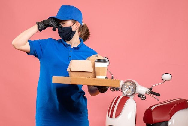 Free photo front view female courier in mask with delivery coffee and food on pink