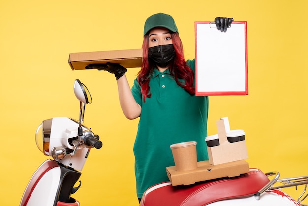 Free Photo front view of female courier in mask with delivery coffee and food on the yellow wall