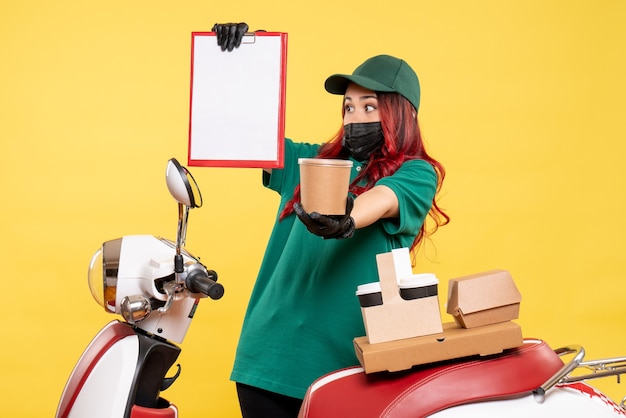 Free photo front view of female courier in mask with delivery coffee and food on yellow wall