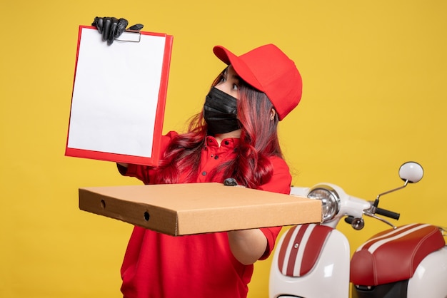 Free photo front view of female courier in mask with delivery food box and file note on the yellow wall