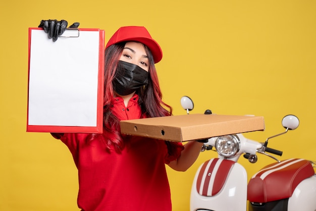 Free photo front view of female courier in mask with delivery food box and file note on yellow wall