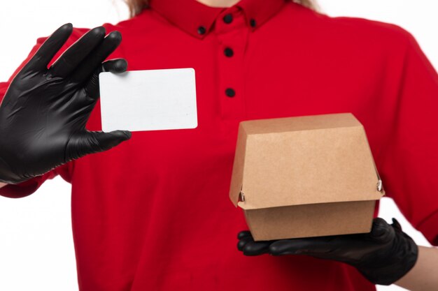 A front view female courier in red shirt black gloves holding white card package on white