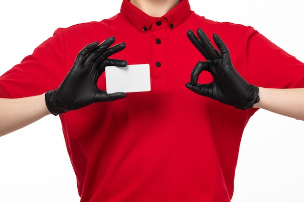 A front view female courier in red shirt and black gloves holding white card posing on white