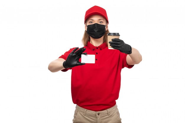 A front view female courier in red shirt black gloves red cap black mask holding coffee and white card on white