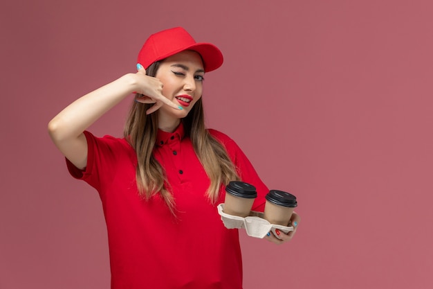 Free Photo front view female courier in red uniform holding brown delivery coffee cups on light-pink background service delivery uniform company