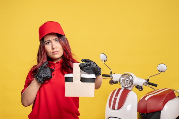 Free photo front view of female courier in red uniform with coffee on yellow wall