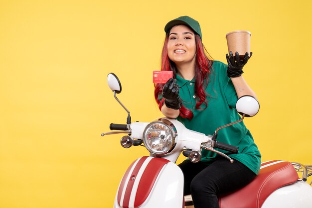 Front view of female courier with dessert and bank card on the yellow wall