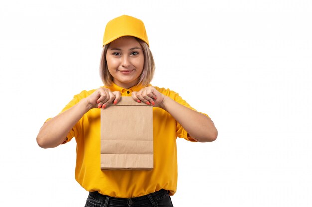 A front view female courier in yellow shirt yellow cap and black jeans holding package food and smiling on white