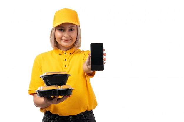 Free photo a front view female courier in yellow shirt and yellow cap holding bowls with food smartphone smiling on white