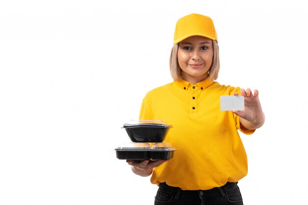 A front view female courier in yellow shirt and yellow cap holding bowls with food and white card o nnthe white