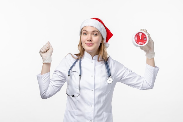 Front view of female doctor holding clock on white wall