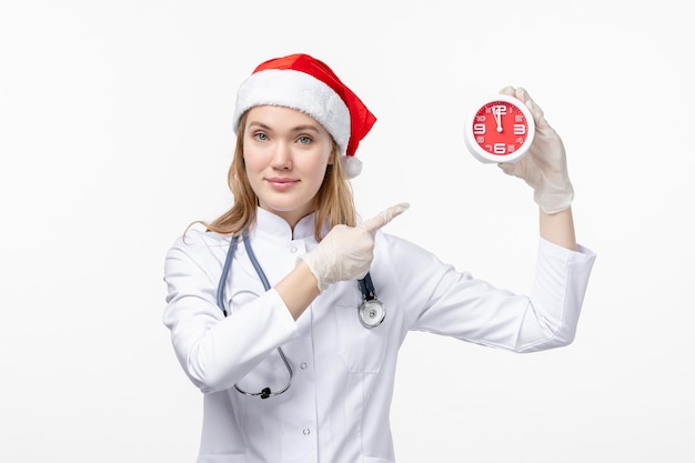 Front view of female doctor holding clock on white wall