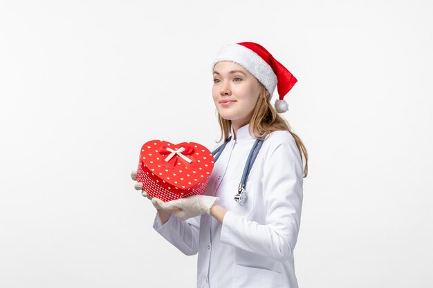 Front view of female doctor holding holiday present on the white wall