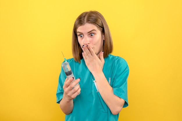 Front view female doctor holding huge injection on a yellow space