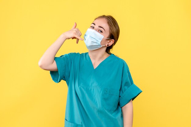 Front view female doctor in mask on a yellow background pandemic covid health virus