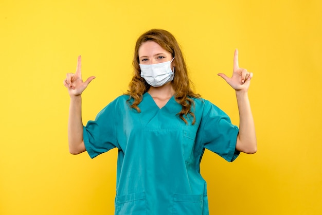 Front view of female doctor in mask on yellow wall