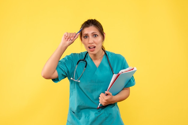 Free photo front view female doctor in medical shirt holding analysis on a yellow background