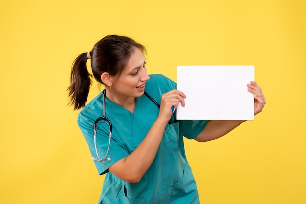 Free Photo front view female doctor in medical shirt holding paper analysis on yellow background