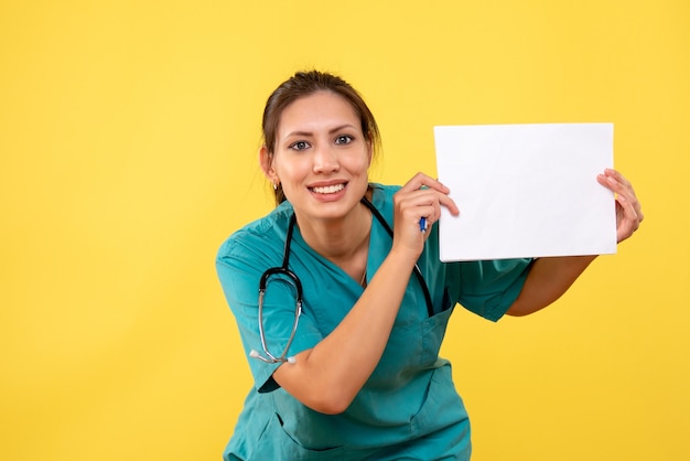 Front view female doctor in medical shirt holding paper analysis on yellow background